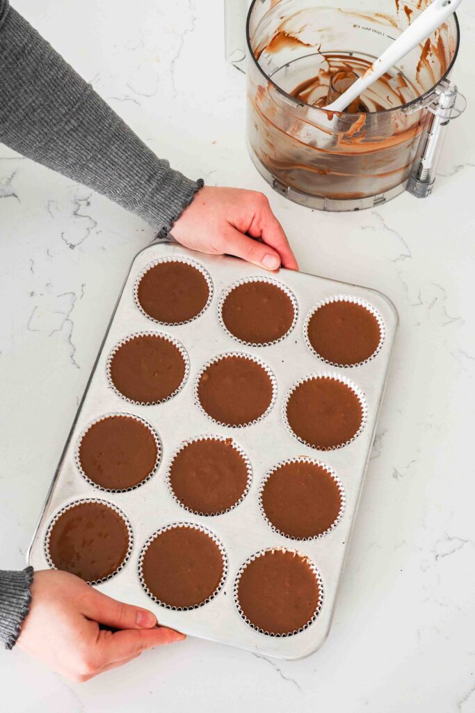 Two hands pick up a tray of unbaked mini chocolate cheesecakes.