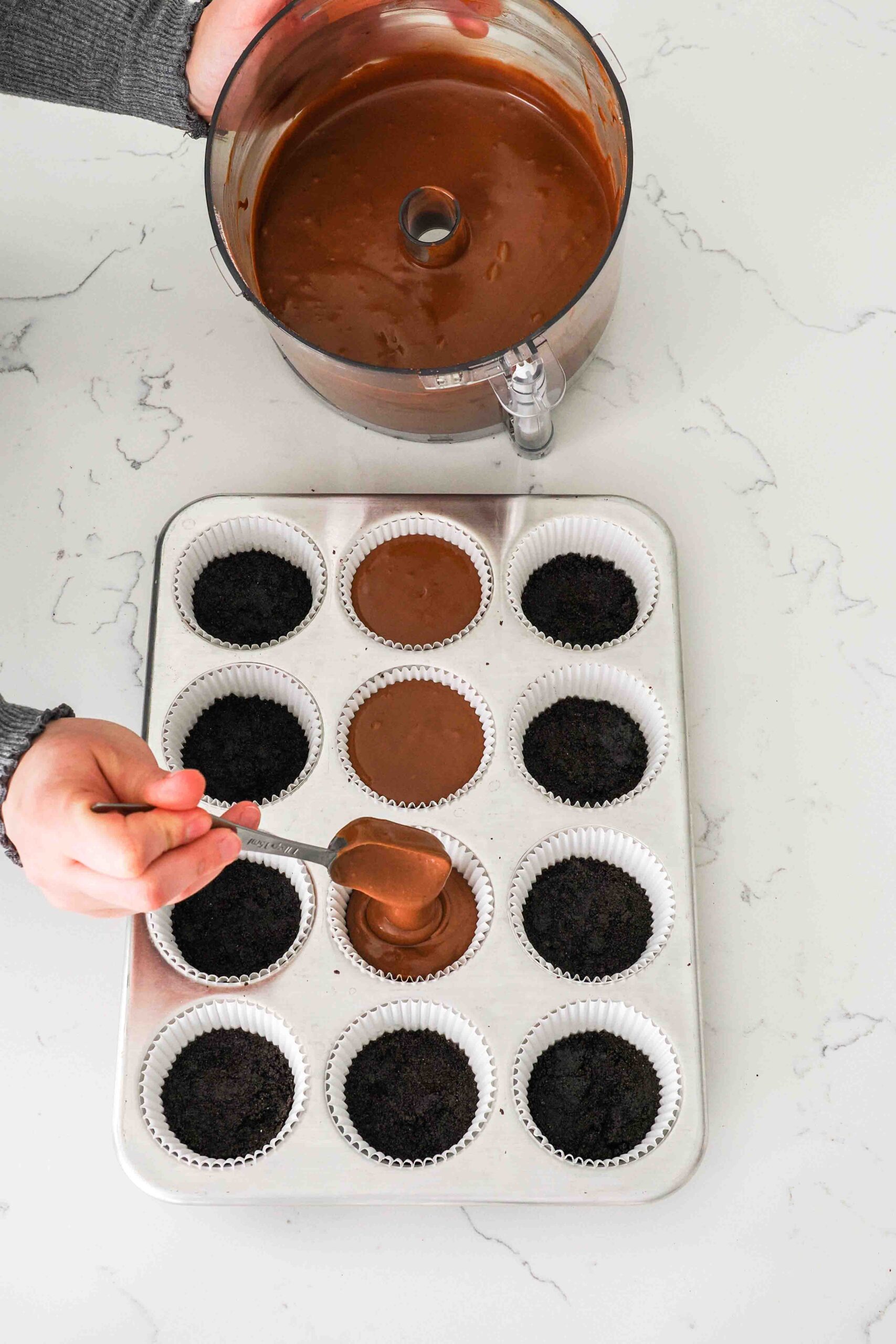 Chocolate cheesecake batter is added to paper liners with Oreo crust in a muffin pan.