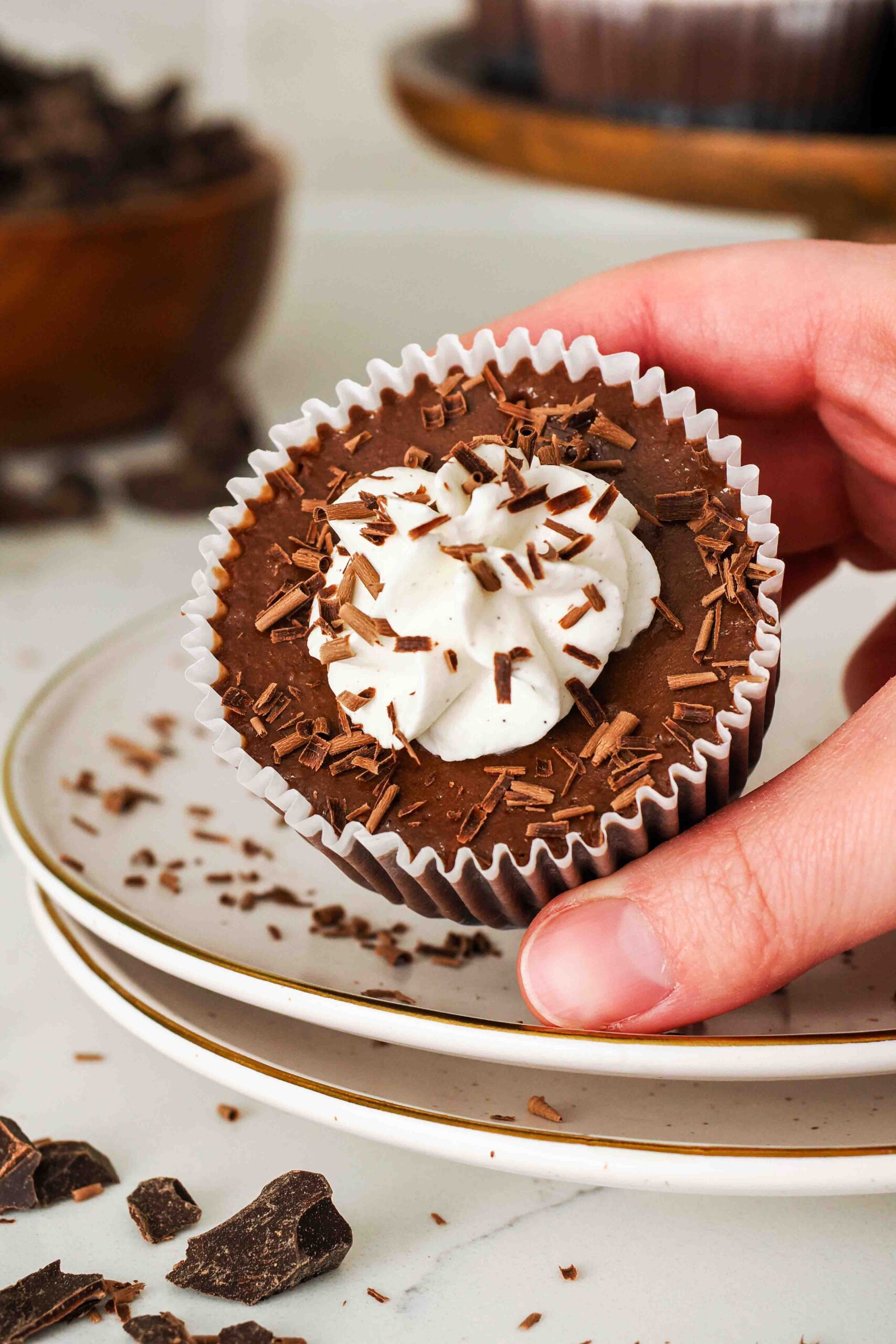 A hand tilts a mini chocolate cheesecake towards the camera.