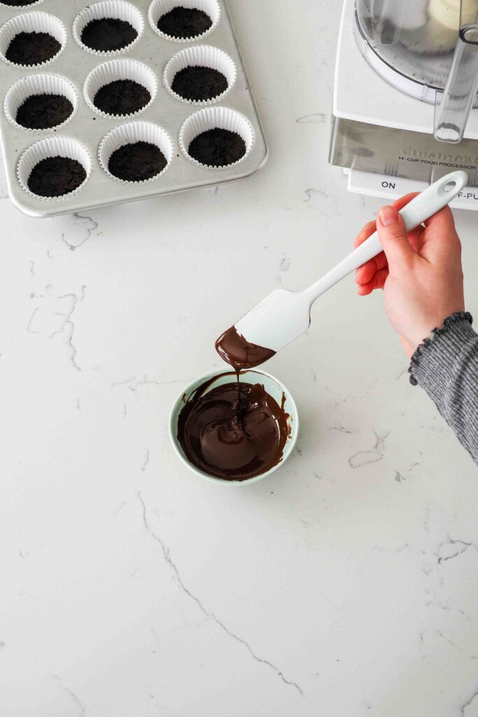Melted chocolate drips off a spatula into a small bowl.