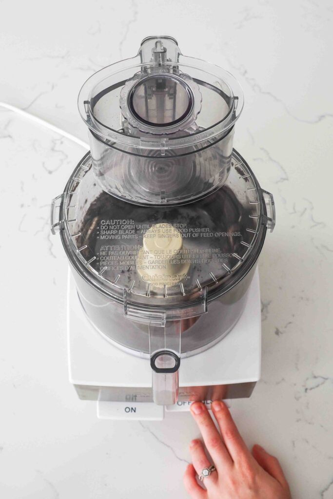 A hand presses "pulse" on a food processor with Oreos.
