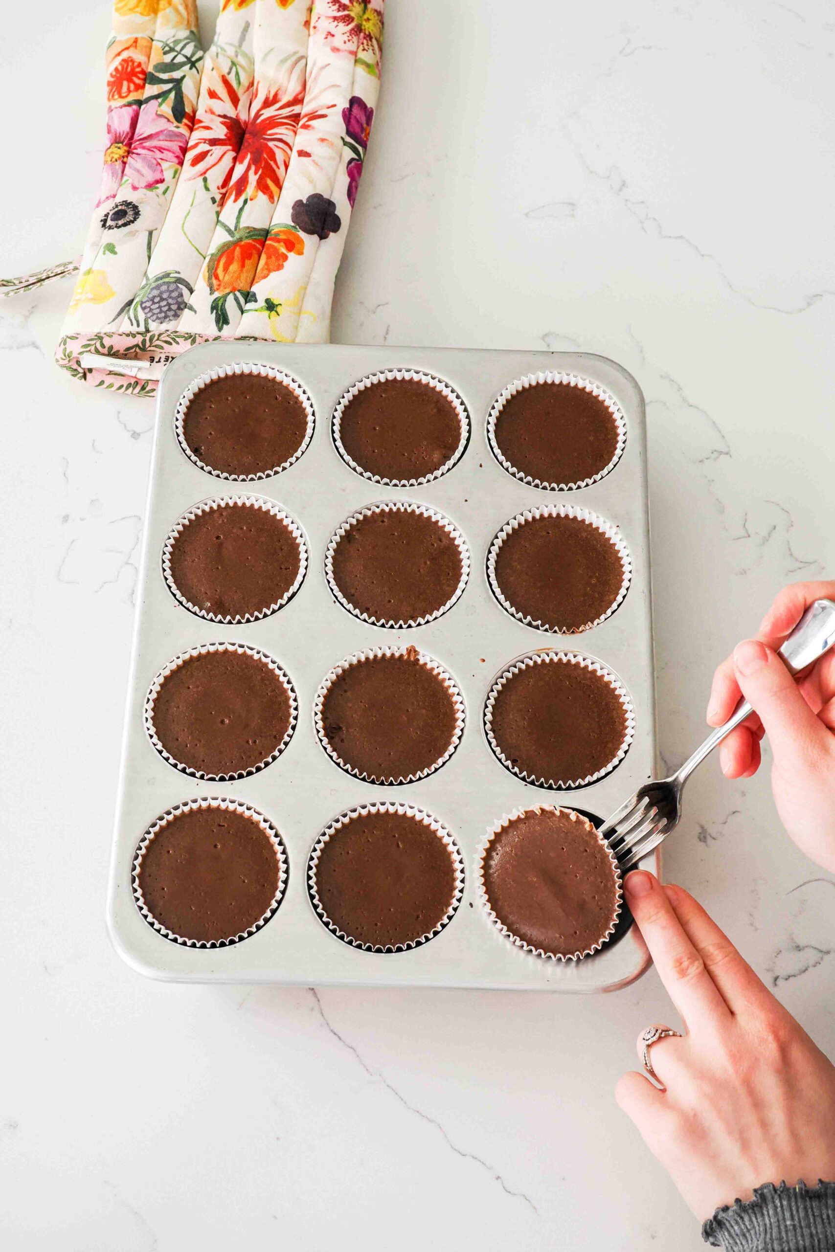Two hands use a fork to tip a mini cheesecake out of a hole in a muffin pan.