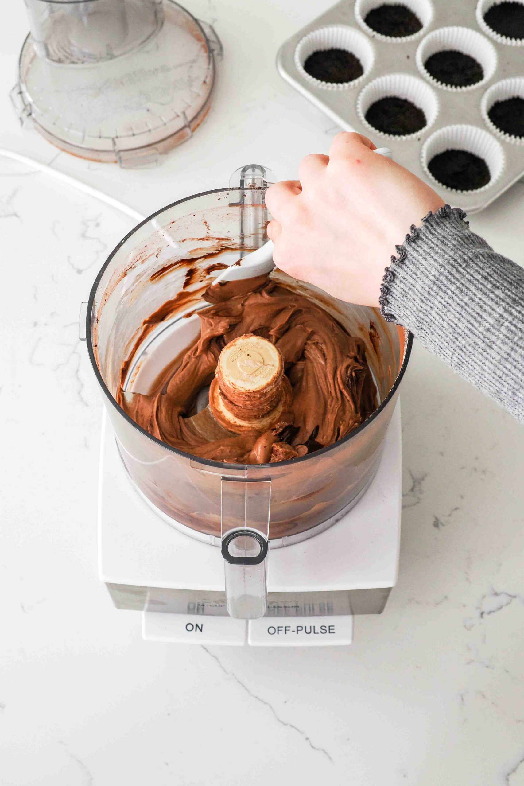 A spatula scrapes down the inside of a food processor bowl with chocolate cheesecake.