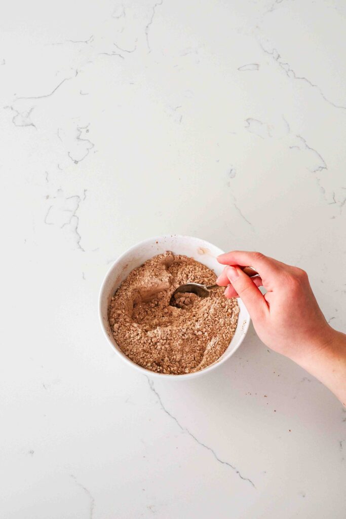 A hand stirs together dry ingredients in a bowl for double chocolate chip cookies.