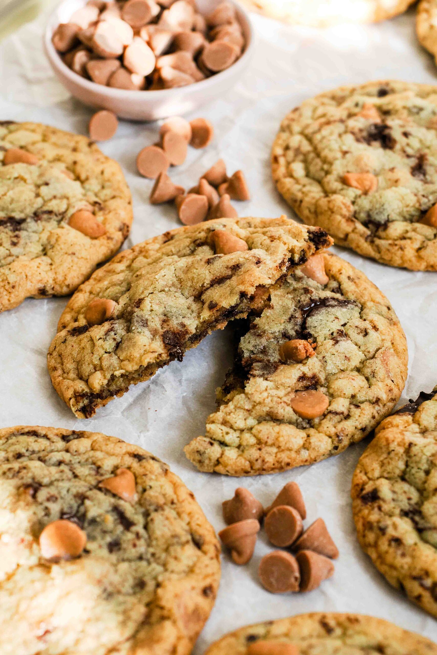 A caramel chocolate chip cookie broken in half on a cookie sheet.