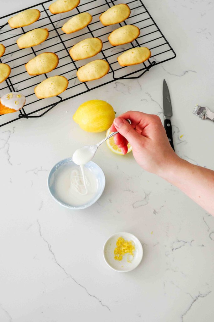 A spoon drizzles thick powdered sugar icing back into a bowl.