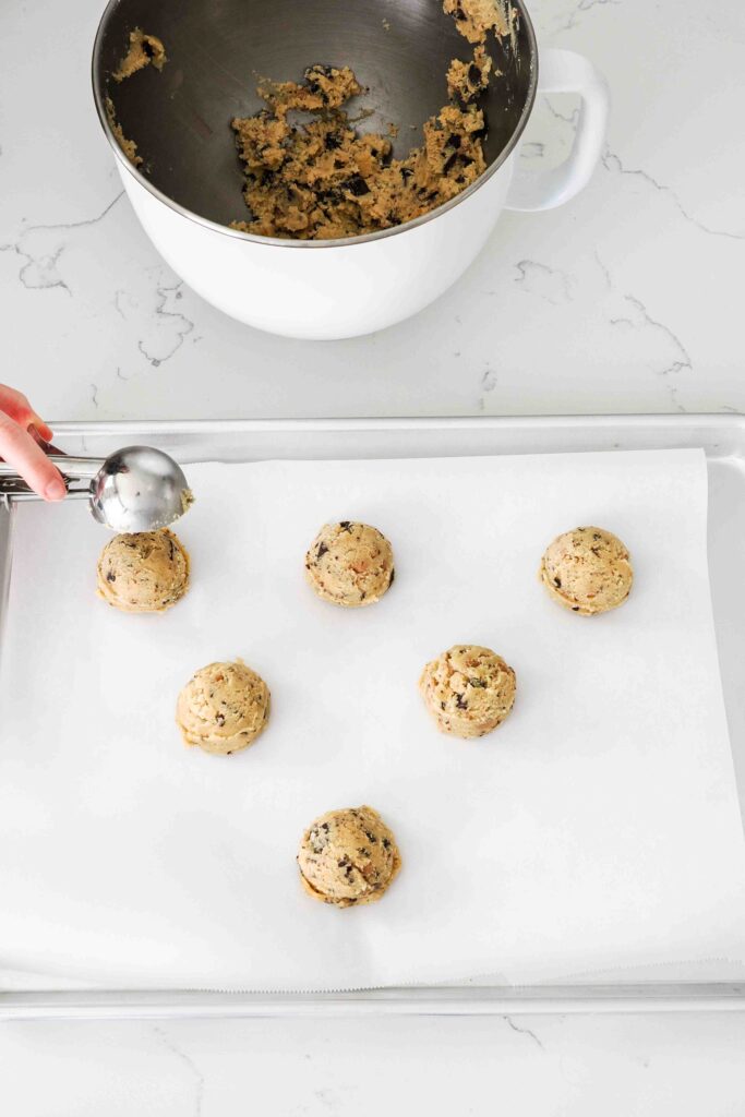 A cookie scoop releases a ball of cookie dough onto a baking sheet.