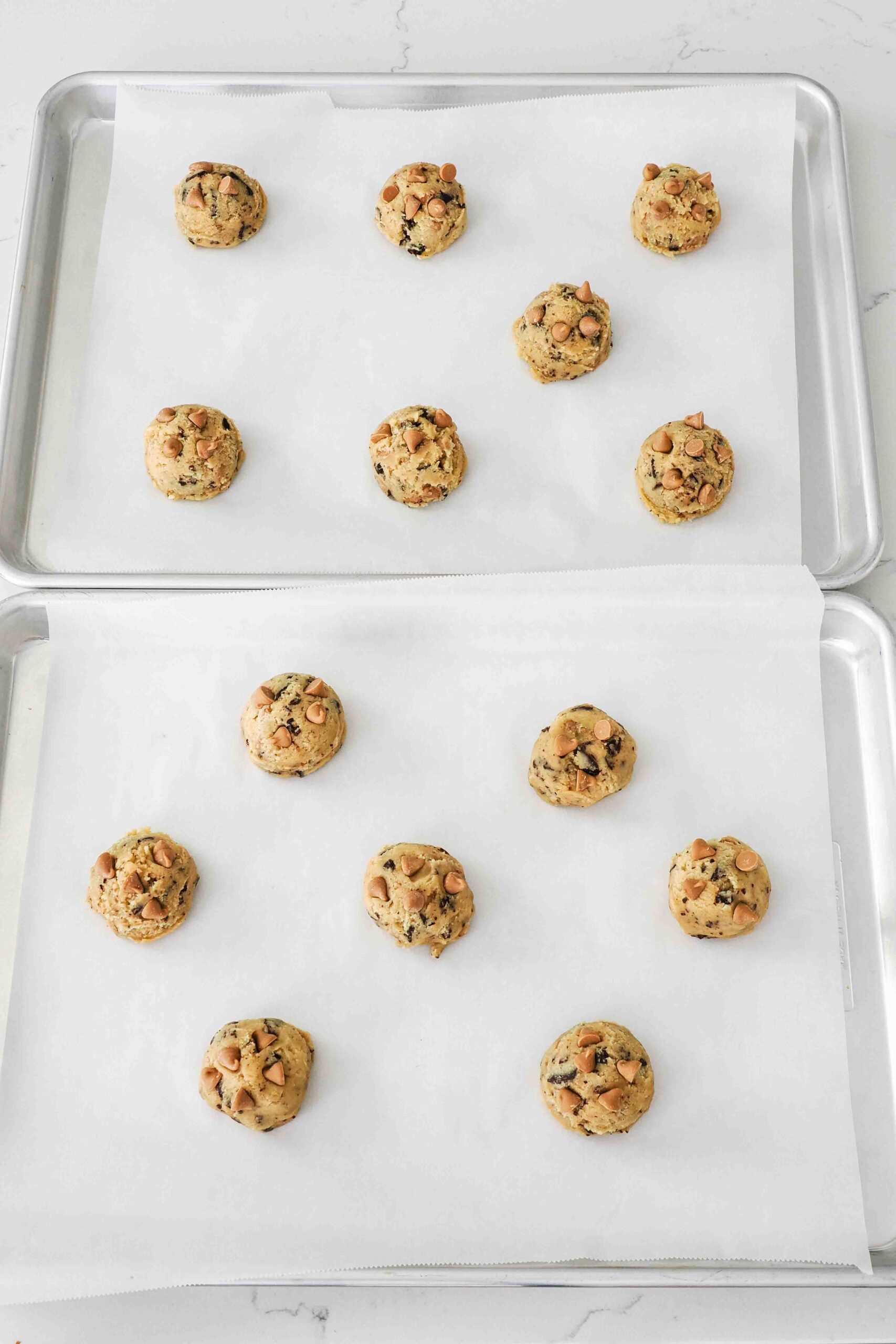 Unbaked caramel chocolate chip cookie dough balls on a baking sheet.