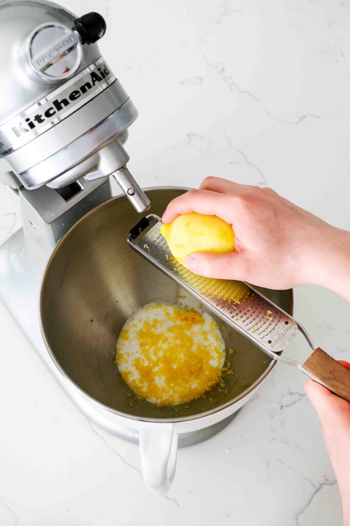 A lemon is zested into a stand mixer bowl with sugar.