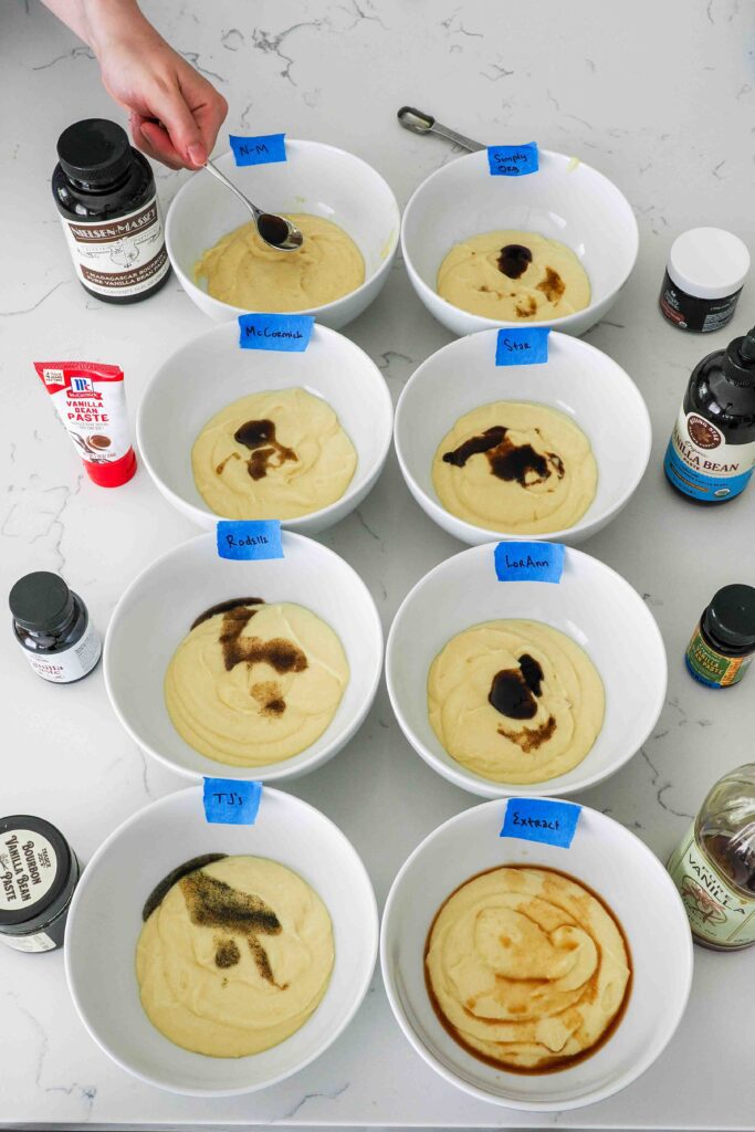 Eight bowls of cake batter with vanilla bean paste on top.