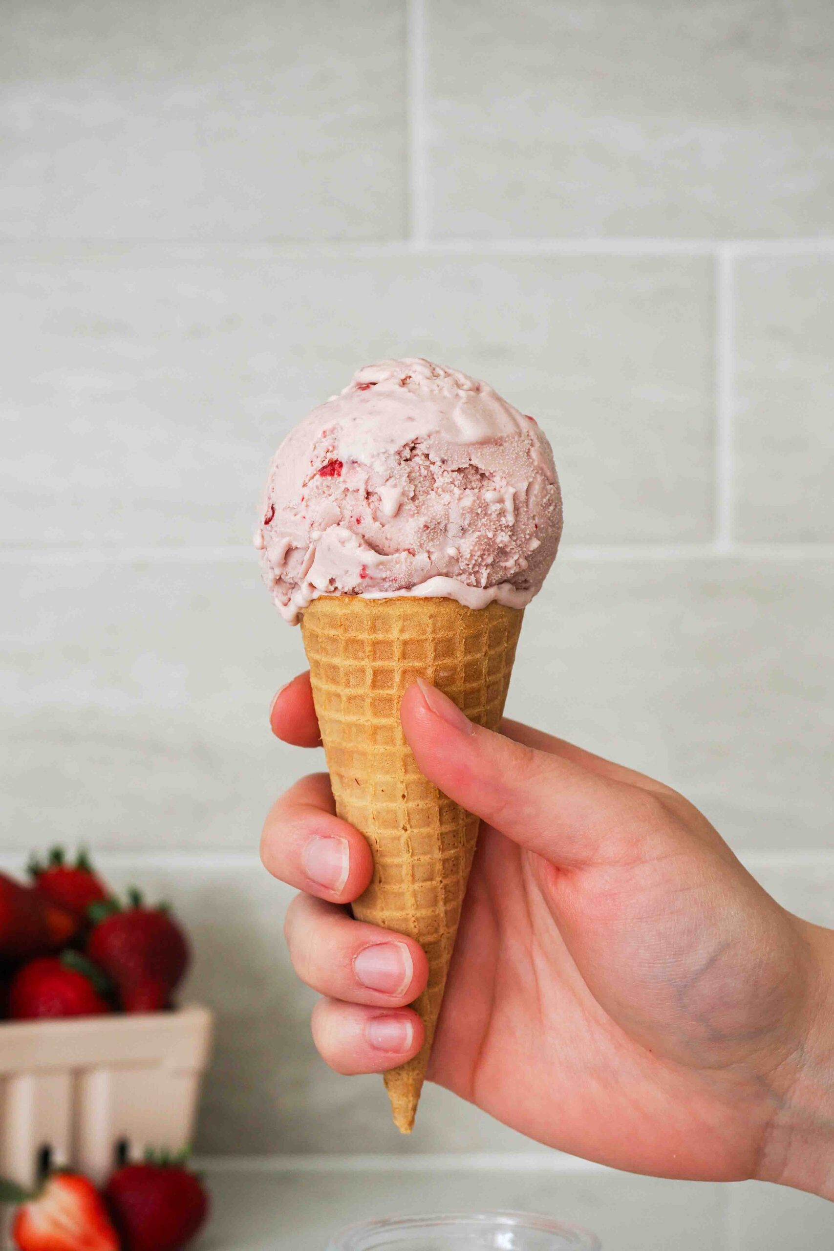 A hand holds a strawberry ice cream cone.