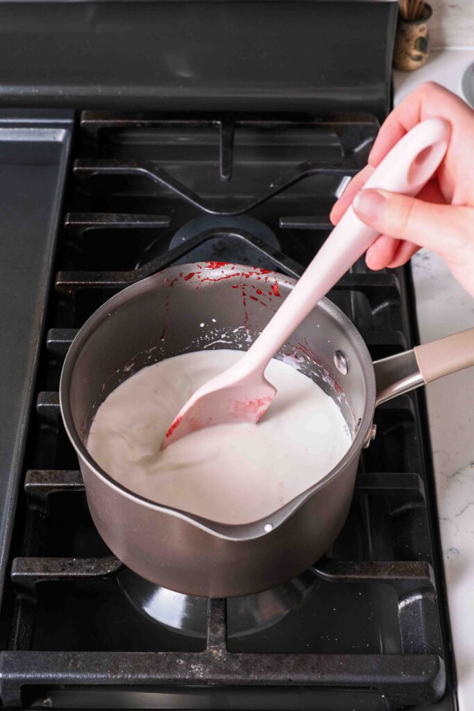 A spatula stirs milk and cream in a medium pot over medium heat.
