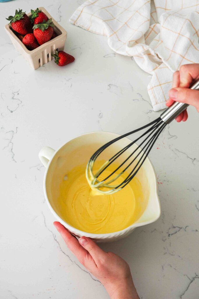 Ribboned egg yolks drip off of a whisk and back into a bowl of batter