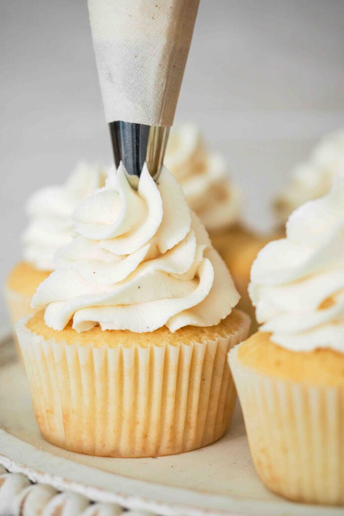 Vanilla bean buttercream is piped onto a vanilla cupcake.