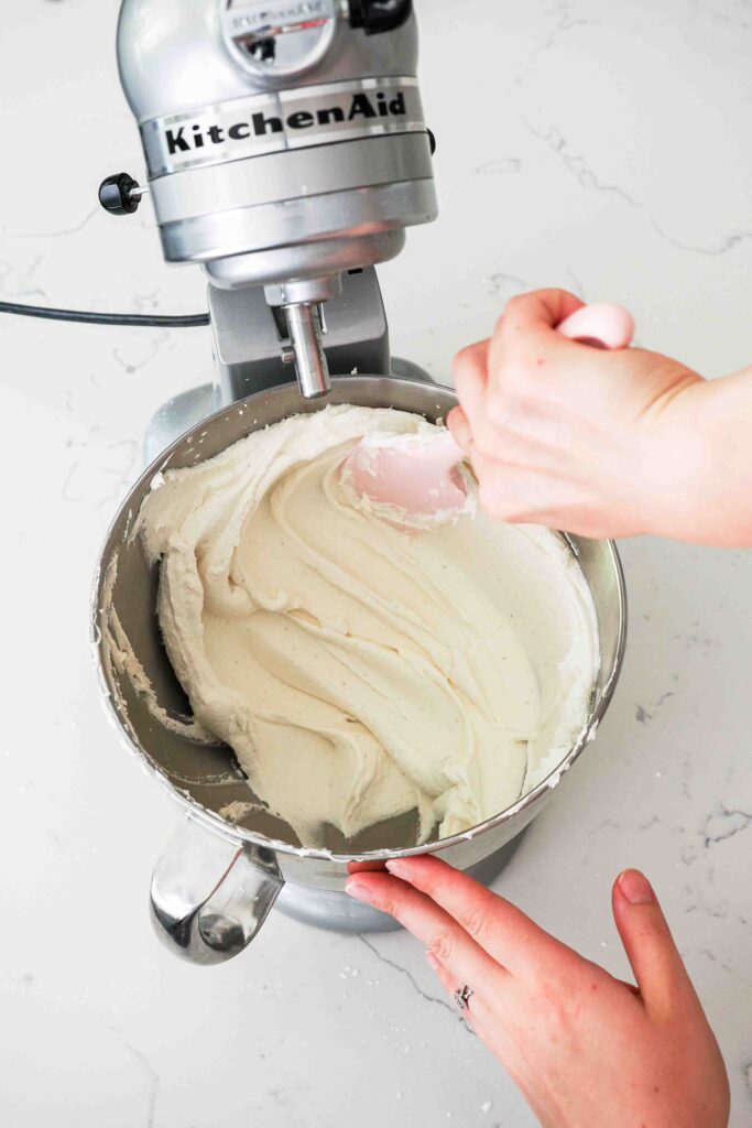 A spatula presses buttercream against the side of a bowl to remove any large air bubbles.