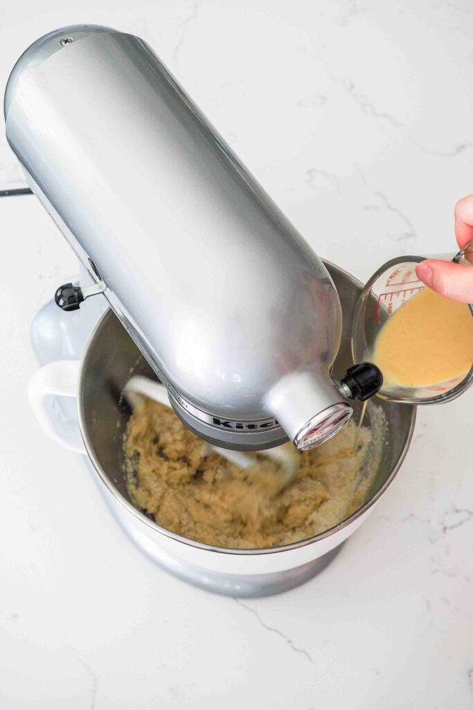 A mixture of egg and milk is poured into the bowl of a stand mixer with dry ingredients.