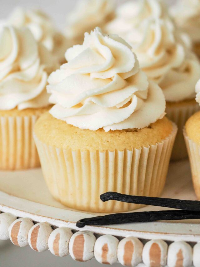 A vanilla cupcake on a cake stand with vanilla beans.