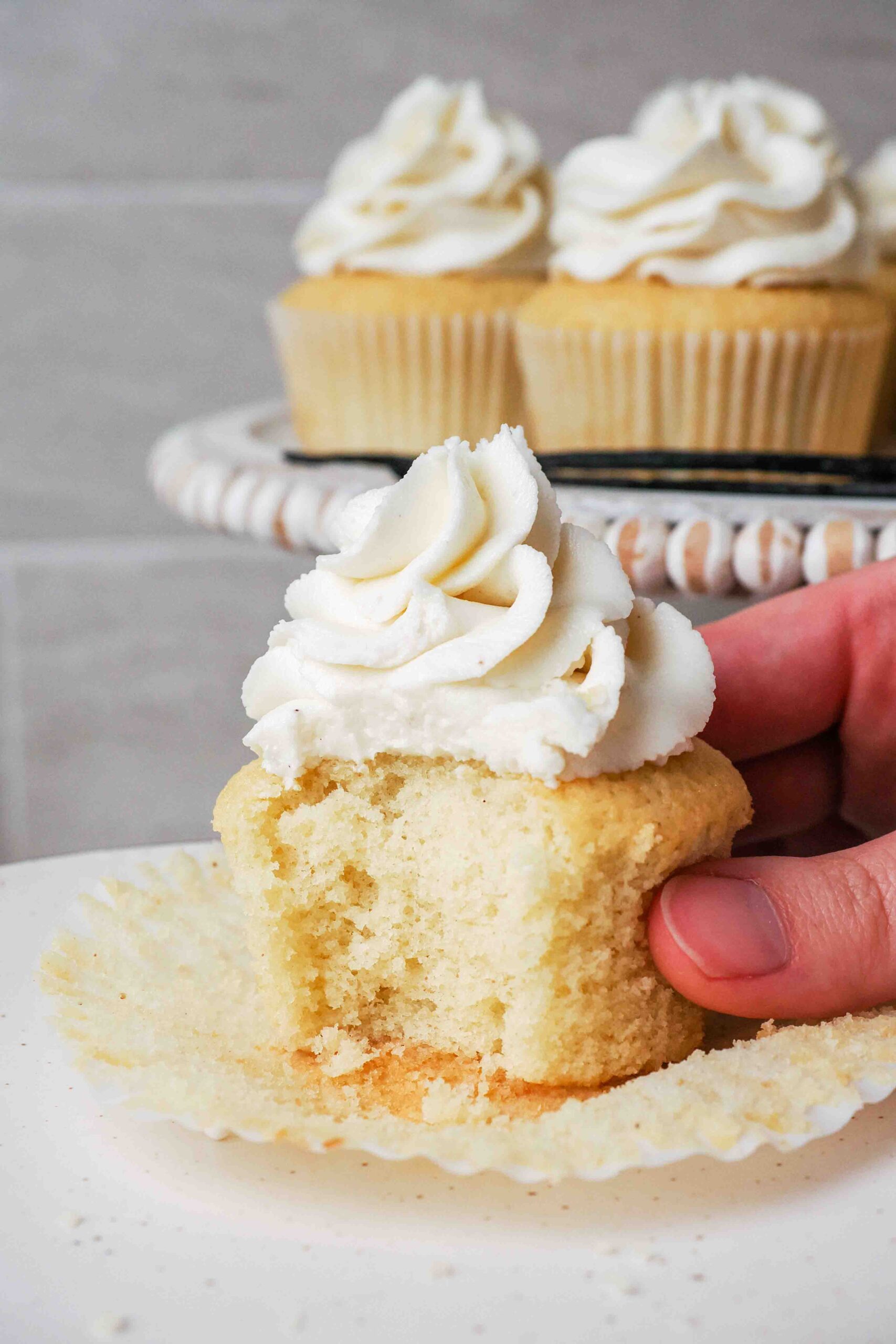 A hand holds a half-eaten vanilla bean cupcake.