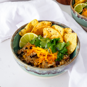 A bowl of brown rice and black bean casserole is topped with tortilla chips and cheddar cheese.