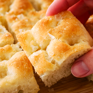 A hand holds up a piece of focaccia bread.