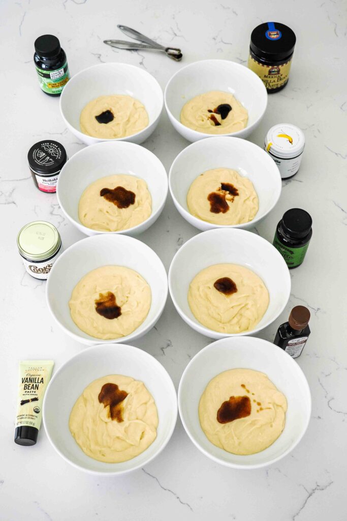 Eight bowls of cake batter with vanilla bean paste on top.