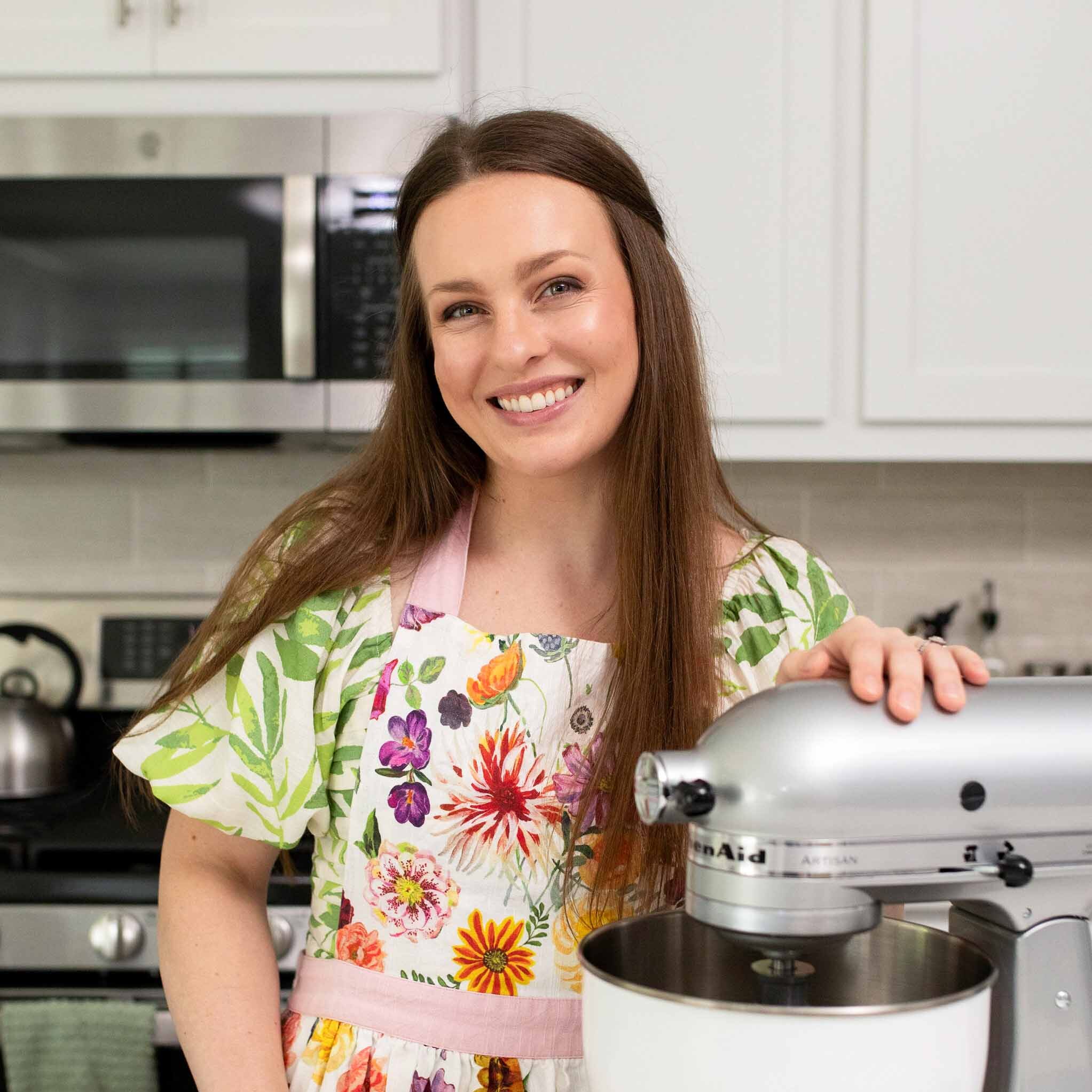 Alyssa, a white woman with brown hair, stands in her kitchen with her hand on a stand mixer.