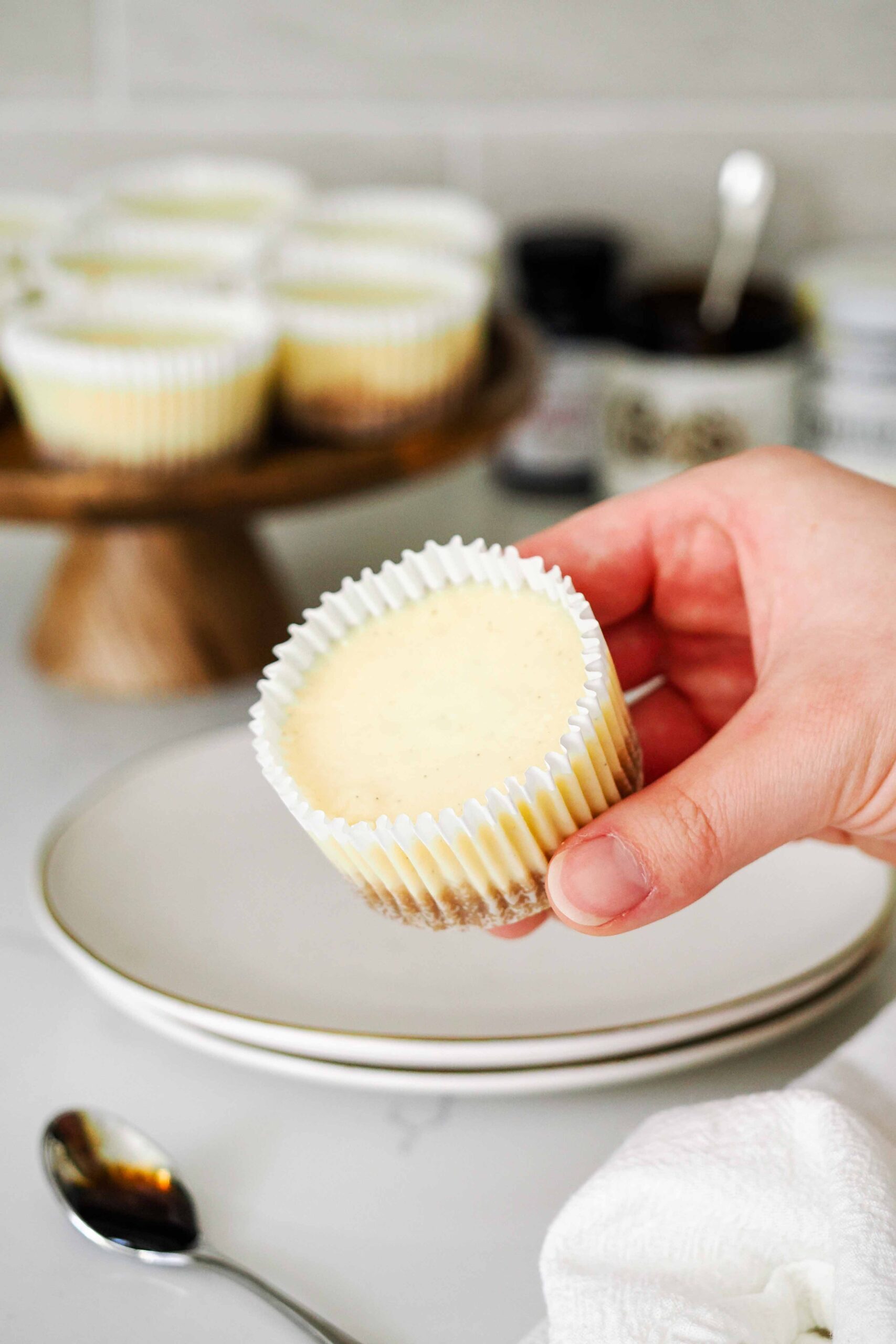A hand holds a mini vanilla cheesecake.