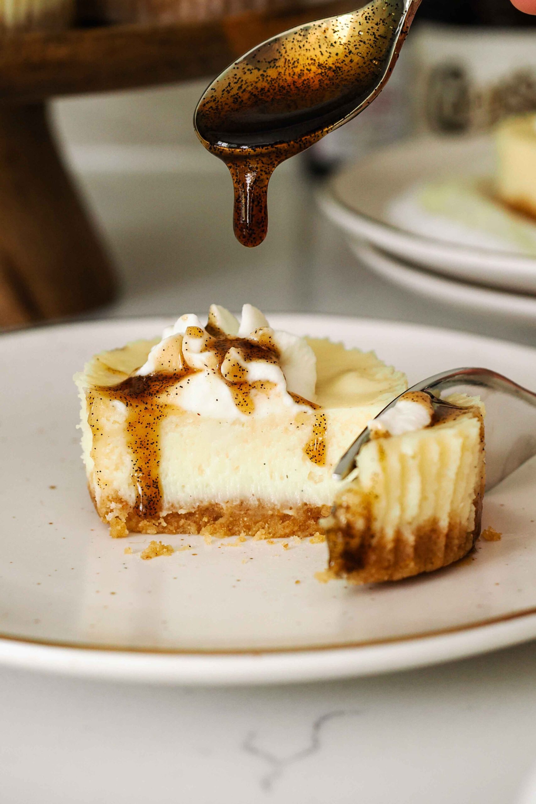 A spoon drips vanilla bean paste onto a mini cheesecake.