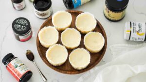 Eight mini cheesecakes on a cake stand with bottles of vanilla bean paste around it.