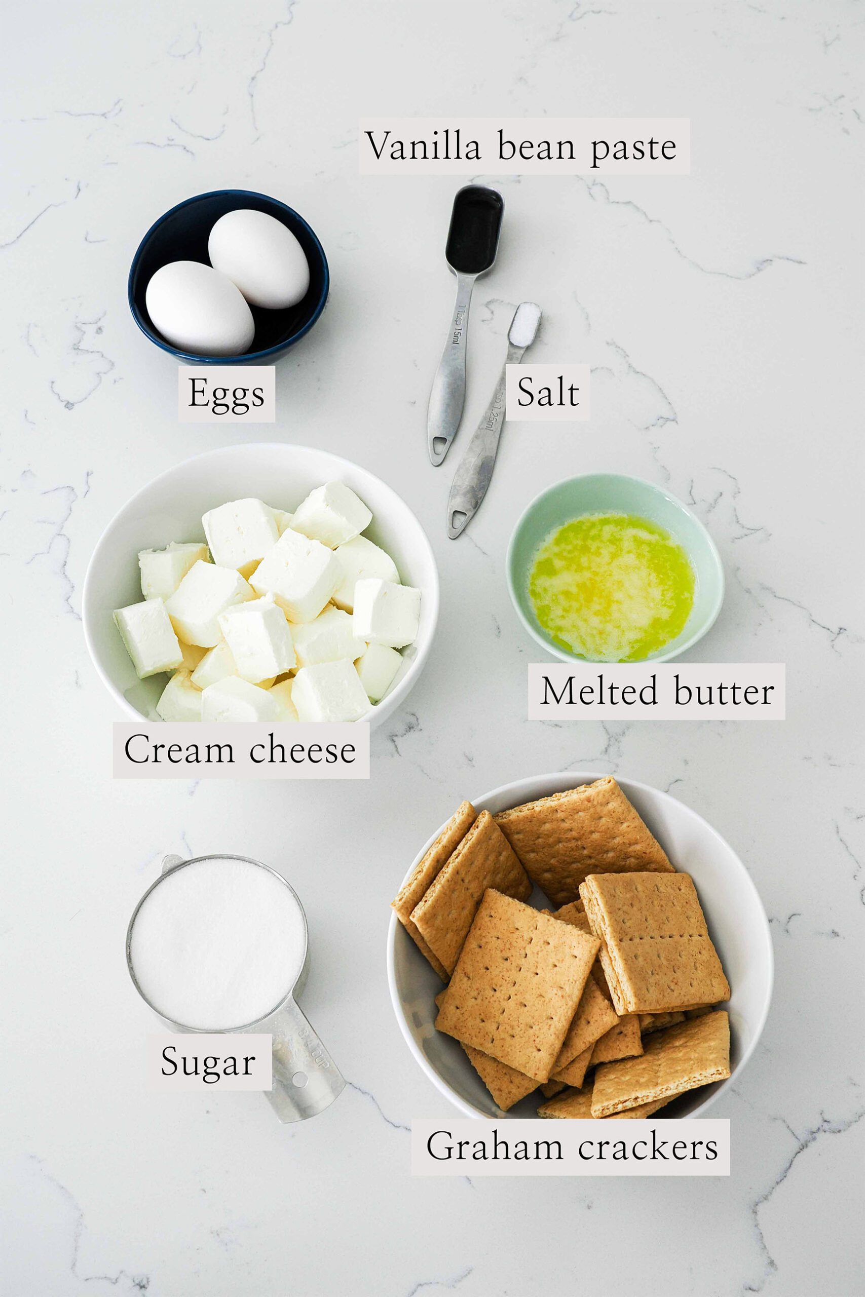 Ingredients for mini vanilla cheesecakes on a quartz counter.