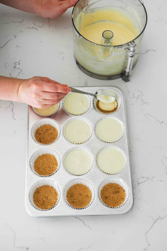 A hand fills mini cheesecakes in a muffin pan.