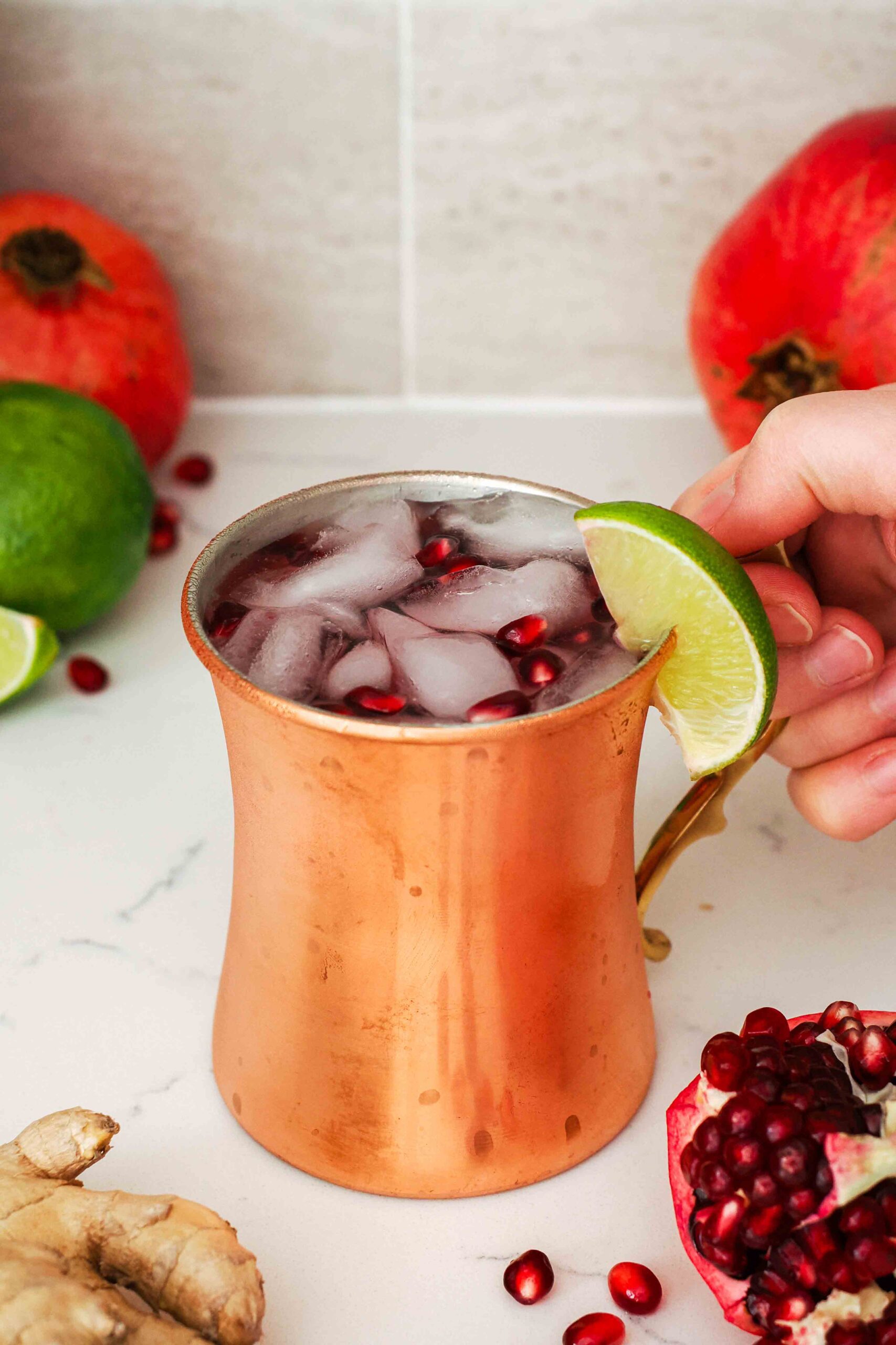 A hand holds a copper mug filled with a pomegranate Moscow mule.