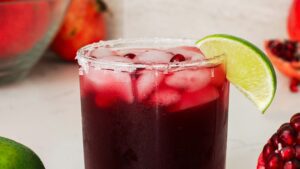 A closeup of a pomegranate margarita glass with a lime wedge.
