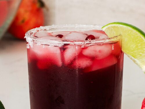 A closeup of a pomegranate margarita glass with a lime wedge.