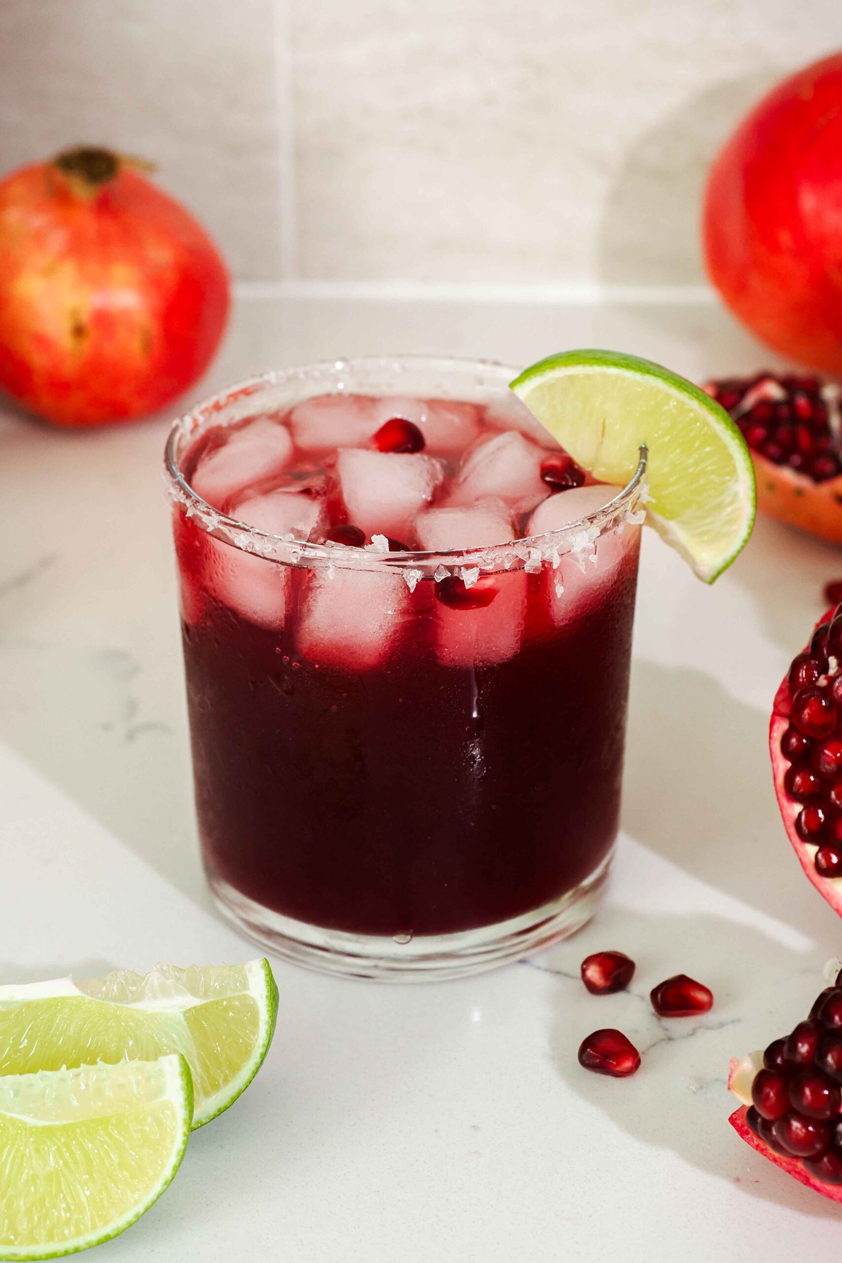 A pomegranate margarita with a flaky salt rim and lime wedge garnish.