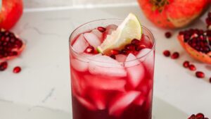 A pomegranate mocktail with a lime wedge and pomegranate arils floating on the top.