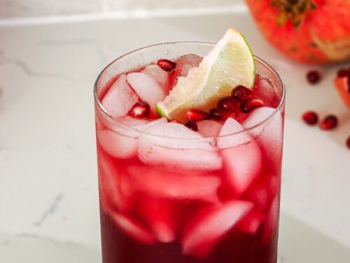 A pomegranate mocktail with a lime wedge and pomegranate arils floating on the top.