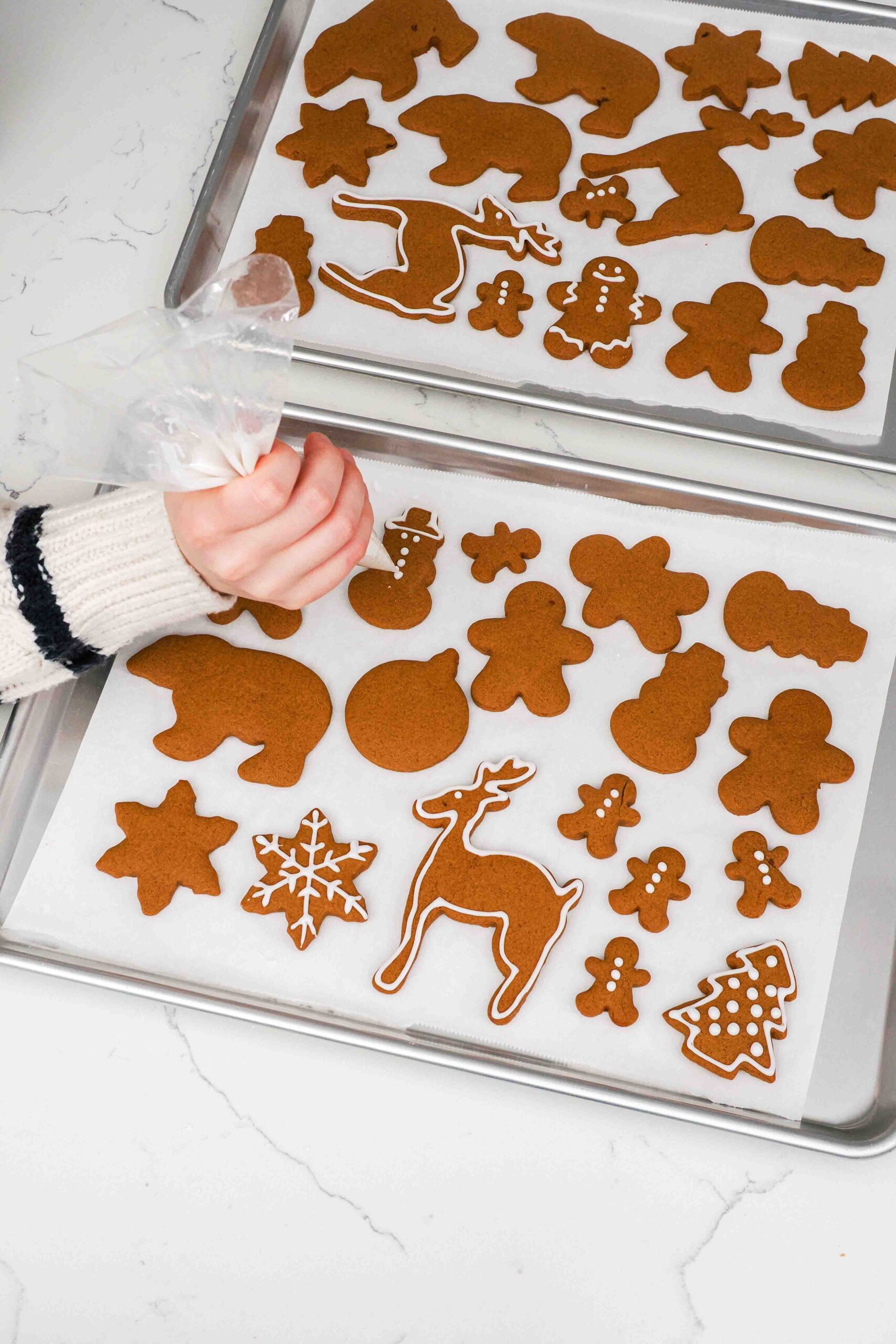 A hand pipes icing onto gingerbread cookies.