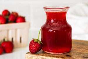 A small glass jar of strawberry syrup with a strawberry.