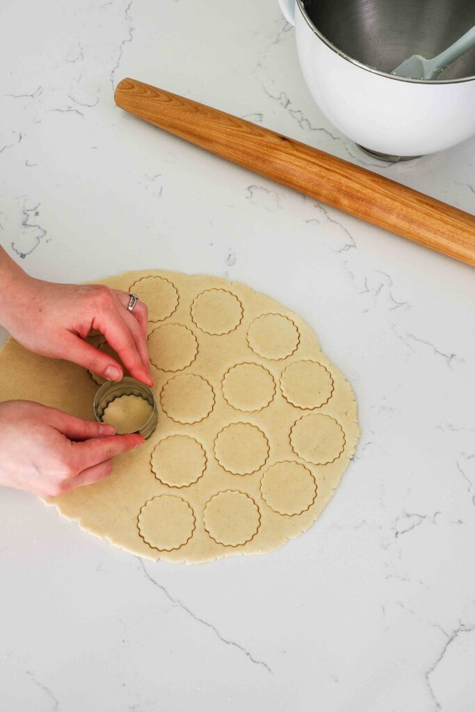 Two hands cut out rounds of vanilla shortbread dough.