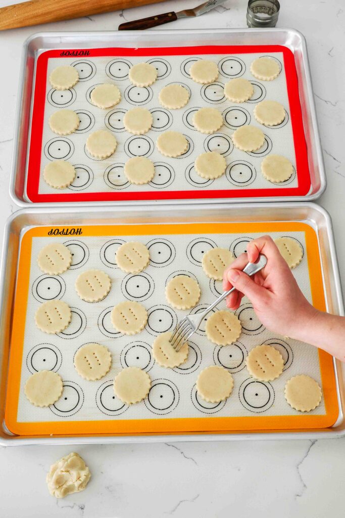 A fork docks shortbread cookies before baking.