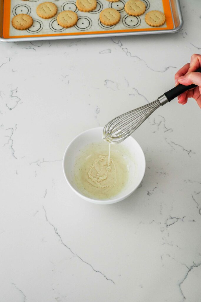Vanilla glaze drizzles off a whisk and into a bowl.