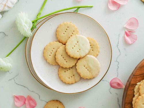 Vanilla shortbread cookies on a plate near flower petals.