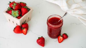A jar of strawberry jam near a basket of strawberries.