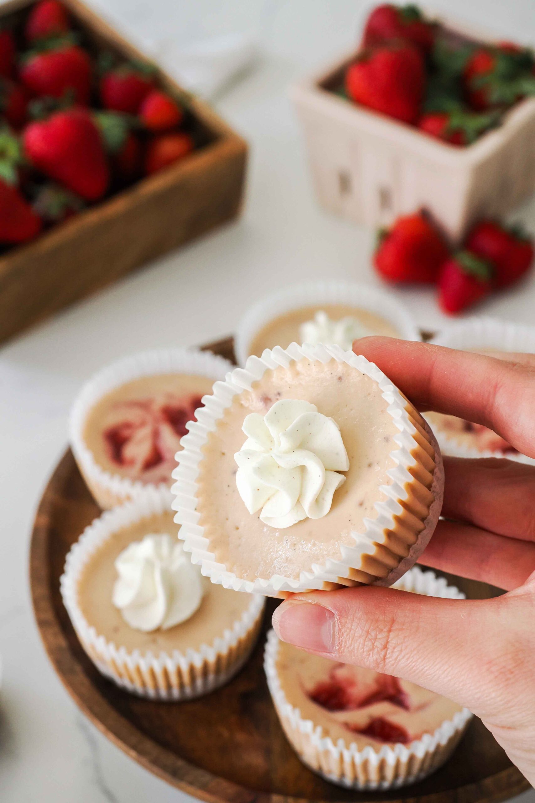 A hand holds up a mini strawberry cheesecake baked in a muffin pan.