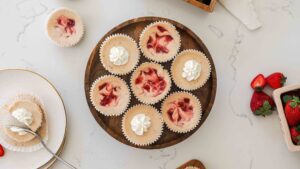 An overhead view of mini strawberry cheesecakes on a wooden cake stand.