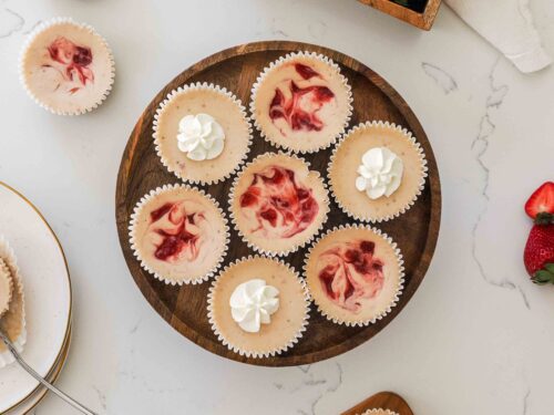An overhead view of mini strawberry cheesecakes on a wooden cake stand.