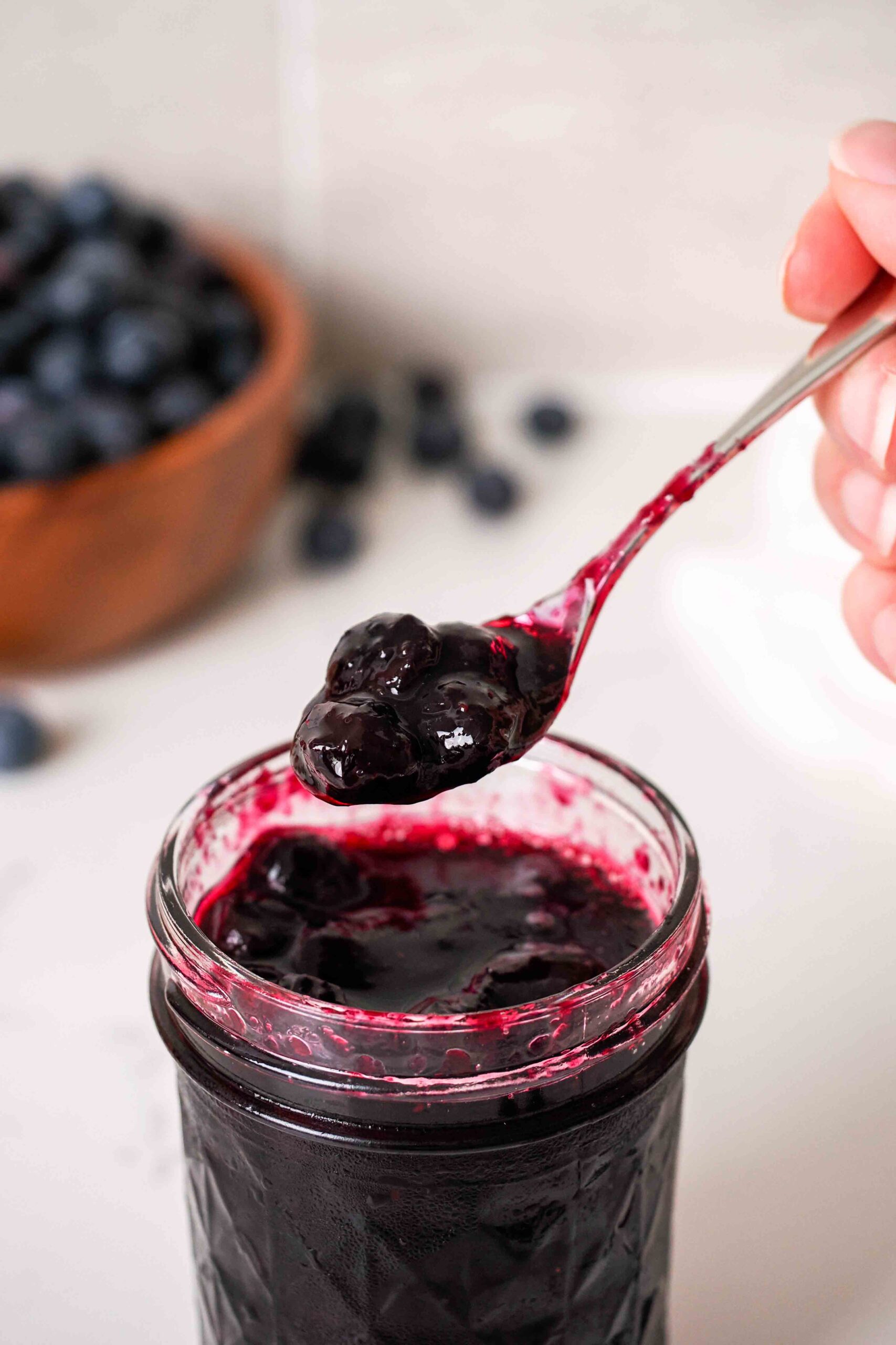 A spoonful of blueberry jam over a jar.