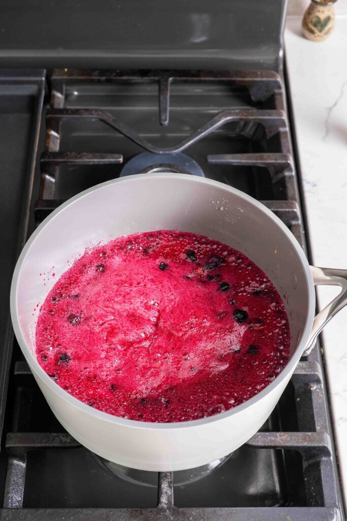 Blueberry jam at a rolling boil in a pot over the stove.