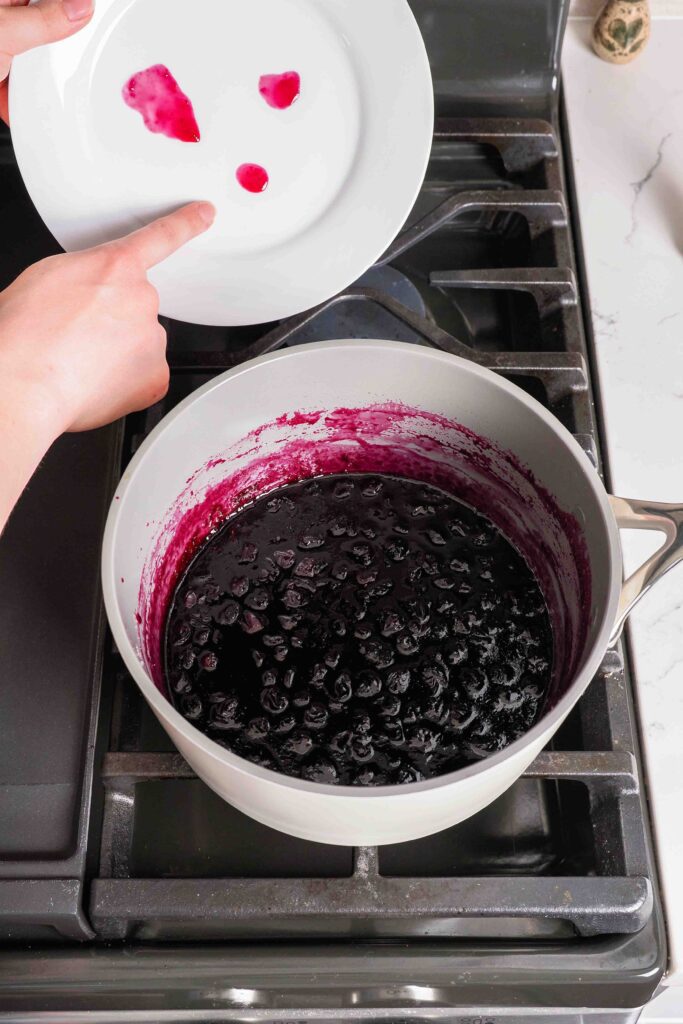 A hand points to gelled blueberry jam on a cool plate above the stove.